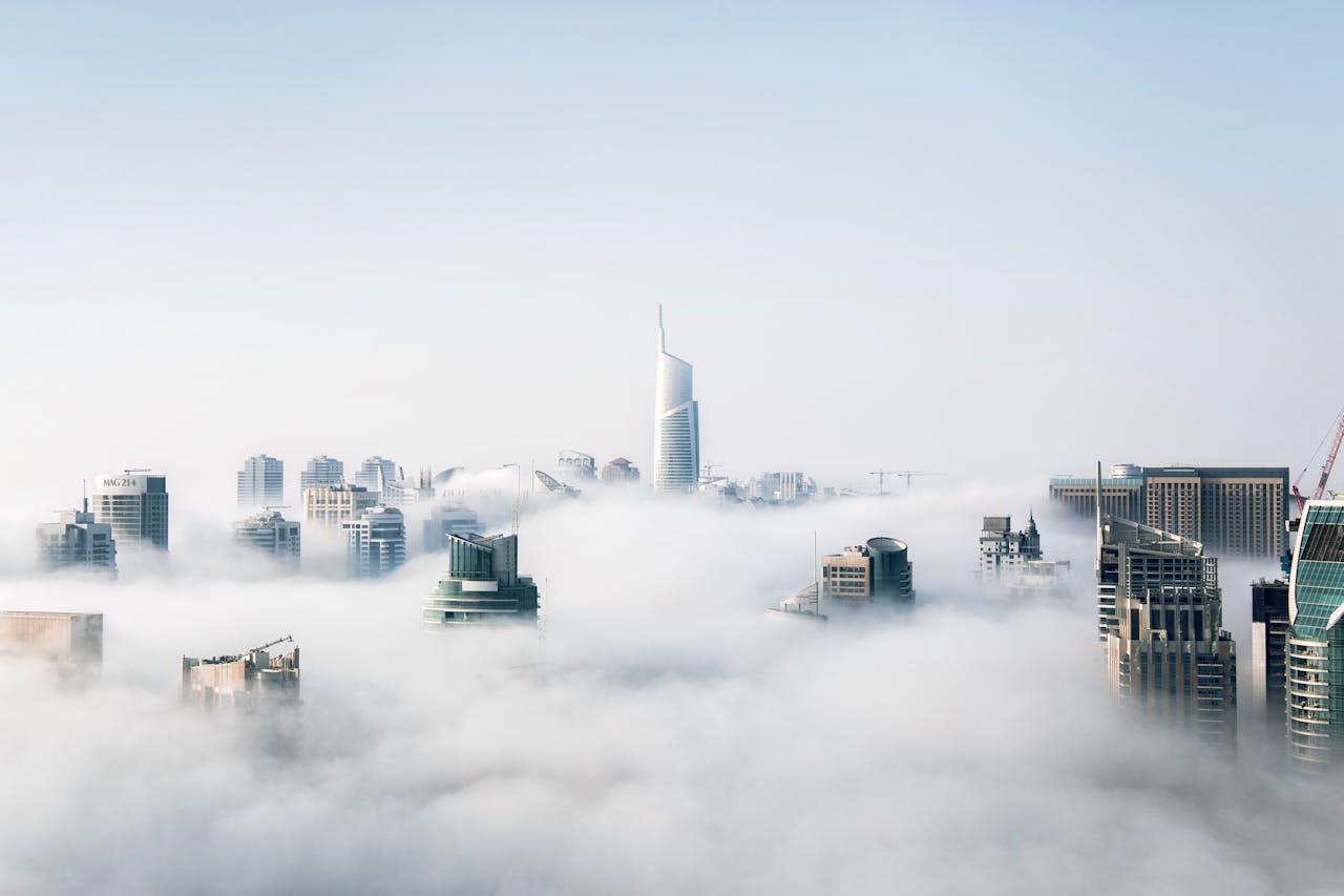 City skyline with tall skyscrapers emerging through thick fog under a clear sky.