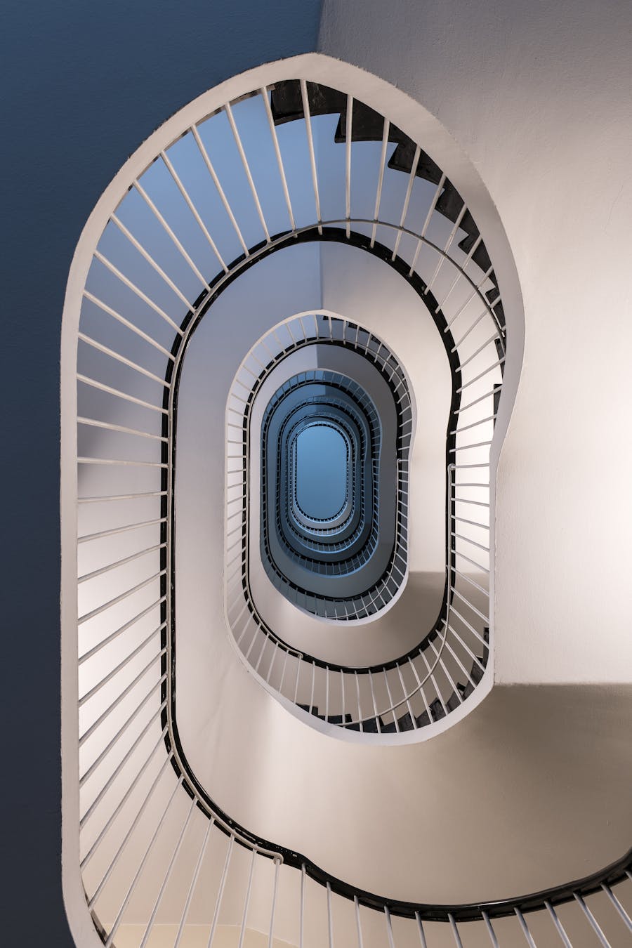 Looking upward through the center of a spiral staircase with white railings and blue walls.